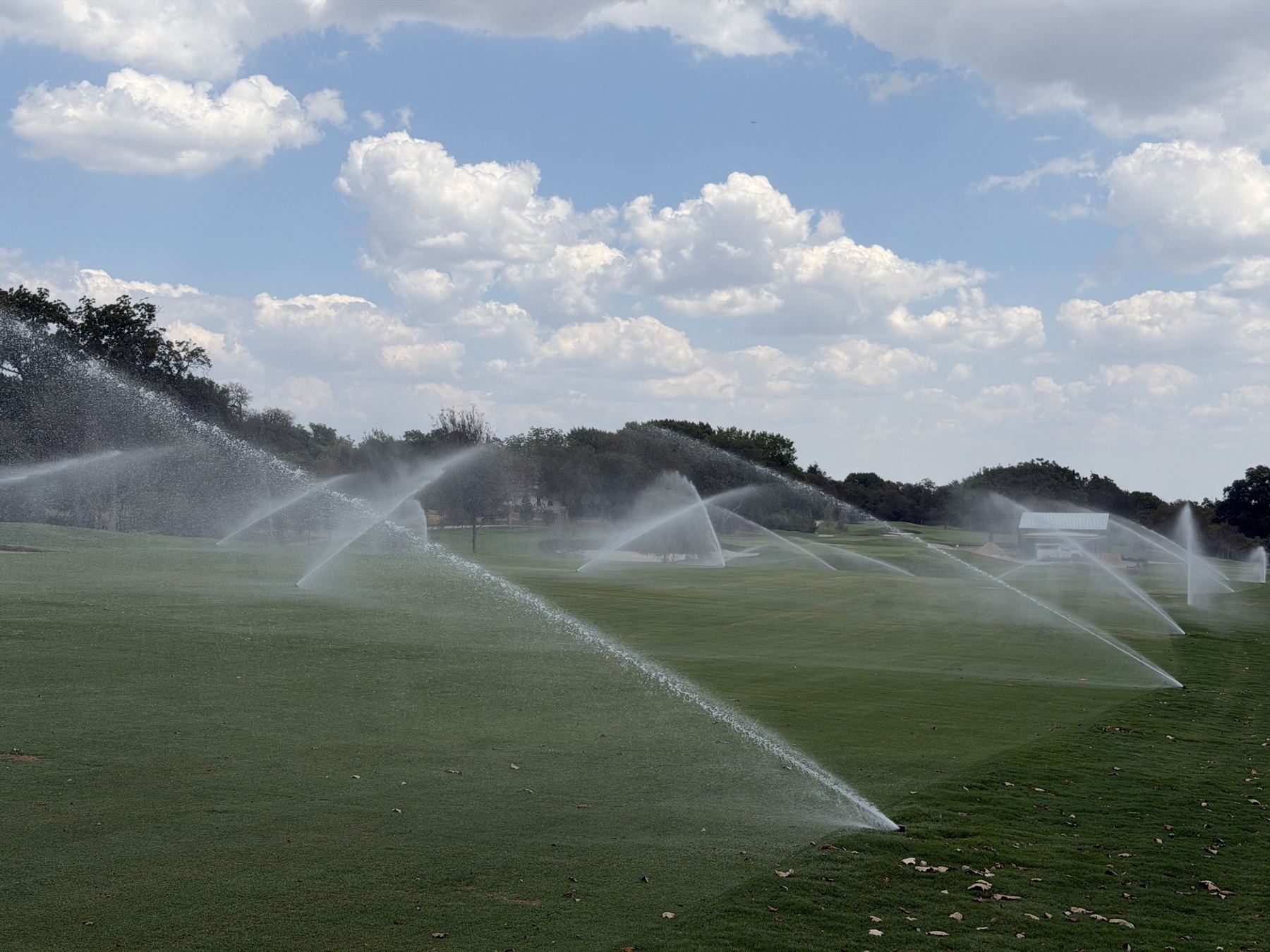 Rotors watering a golf fairway under a blue sky